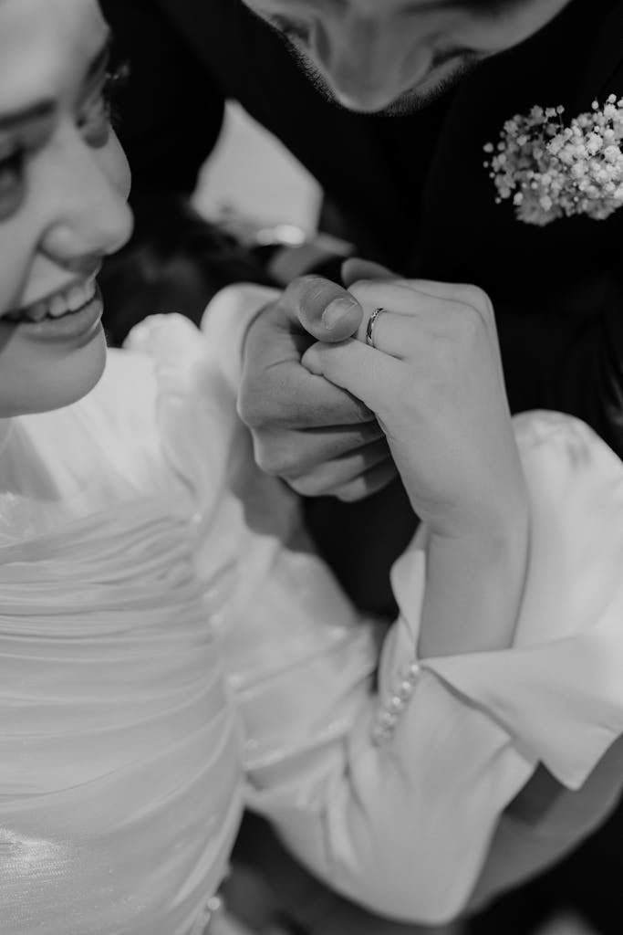 Romantic close-up of a couple holding hands during a wedding, captured in black and white.